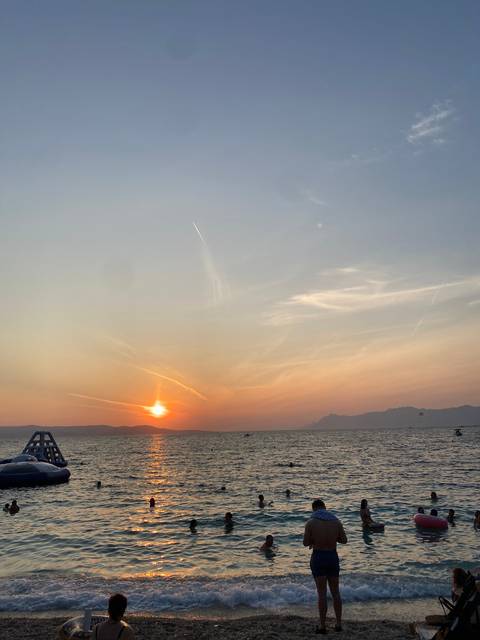       Swimmers enjoying a colorful sunset over the ocean.
  