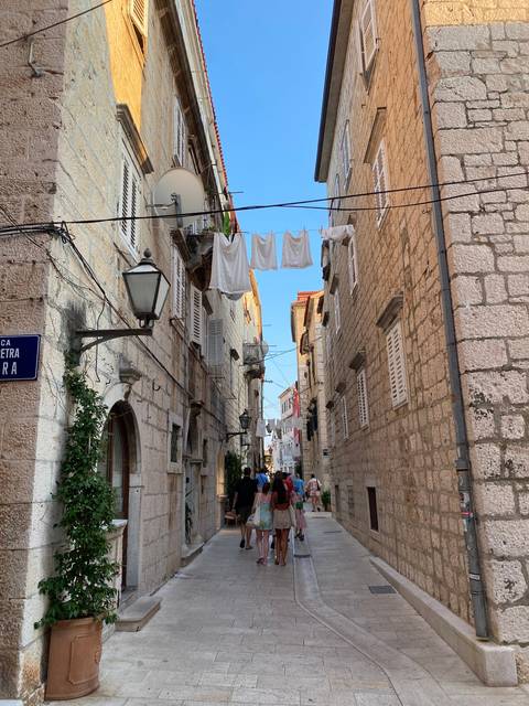       Narrow street with stone buildings, hanging laundry, and tourists.
  