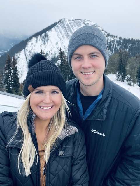       Couple smiling in a snowy mountainous environment.
  