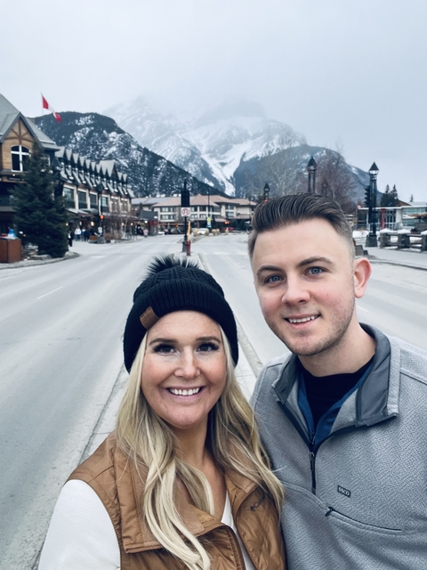       Couple standing in a snowy town with mountains.
  