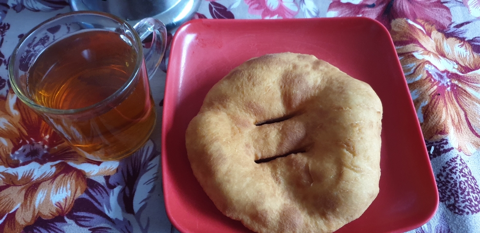 A traditional fried bread and a glass of tea on a table.