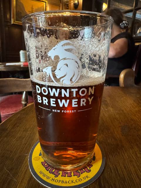 A glass of beer with a brewery logo on a wooden table.