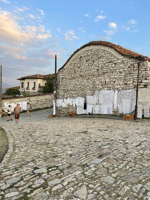 Stone building with hanging laundry and cobblestone ground.
