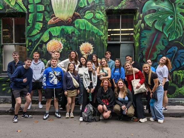       Group of young people posing in front of graffiti-covered walls.
  