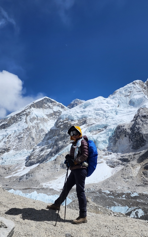       Hiker standing on rocky terrain with mountain backdrop.
  
