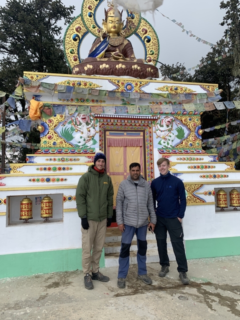 Three people standing in front of a colorful, ornate stupa.
