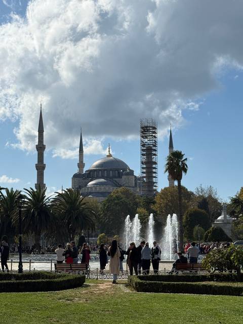      People in a park near a mosque with fountains.
  