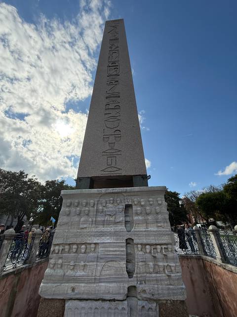       An obelisk with engravings in an outdoor setting.
  