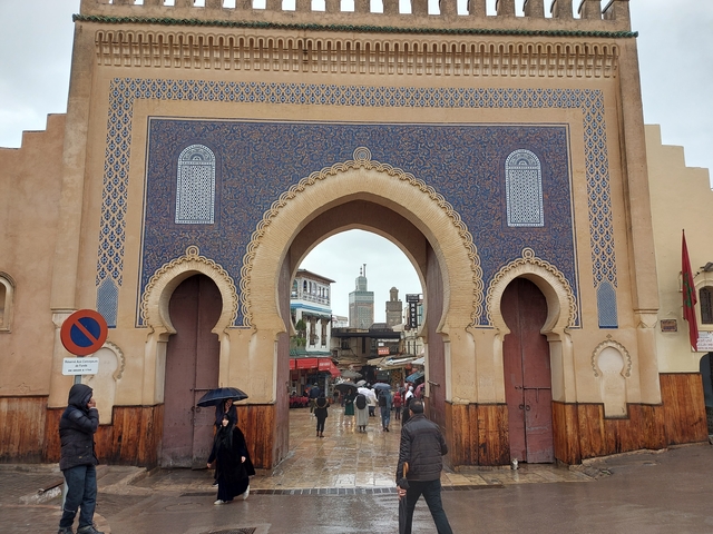 A beautifully designed historic gate with people under umbrellas.