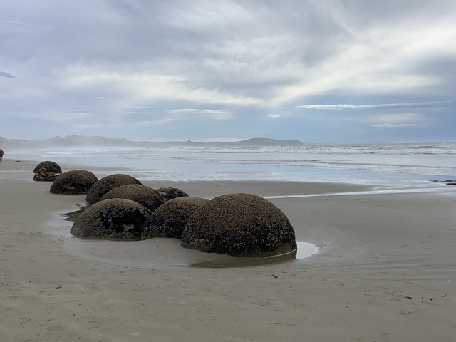       Round boulders on a sandy beach with waves.
  