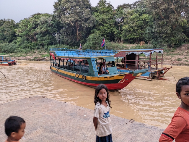       Brightly painted boat on a muddy river with people.
  