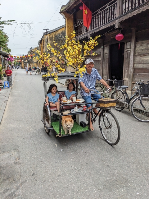       Man riding a bicycle with two children and a dog on a street.
  