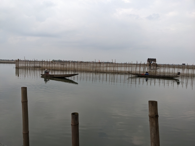       Two people paddling boats on a calm body of water.
  