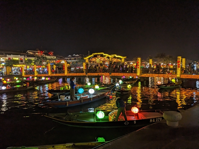       Illuminated boats and a bridge reflected in water at night.
  