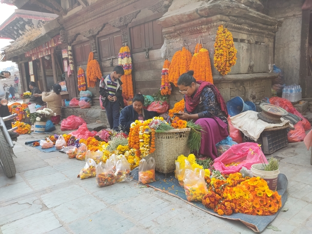       Market scene with people selling and arranging marigold flowers.
  