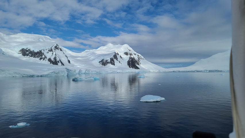 Calm sea with floating icebergs and snowy mountain range.