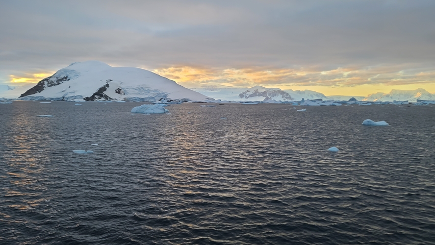 Snow-covered mountains and iceberg-filled ocean under a cloudy sky.
