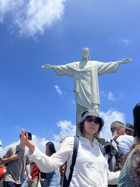       Tourist posing in front of a large statue of Christ the Redeemer.
  