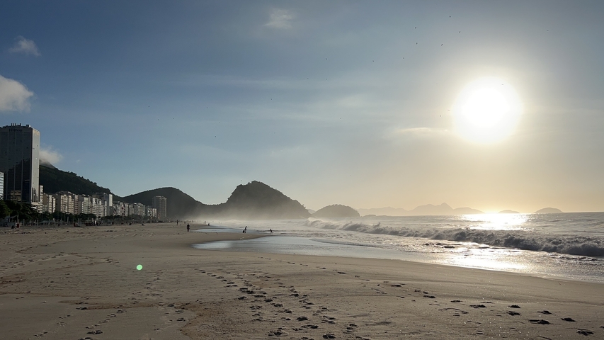       Sandy beach with ocean waves under the setting sun.
  