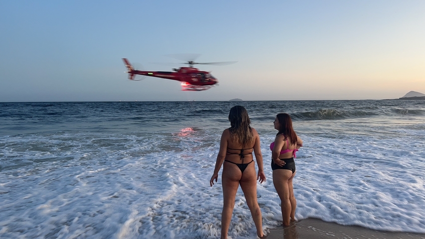       Women watching a helicopter and waves at the beach.
  