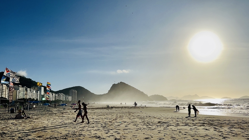 People strolling on a sunlit beach with a clear sky.