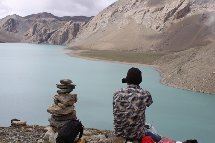 Person sitting by a cairn taking a picture of a glacial lake.