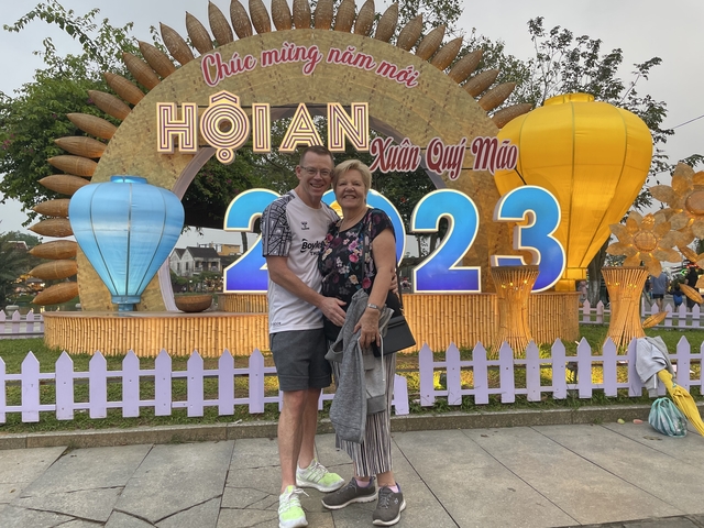       Couple posing in front of a neon-lit sign for a festival in Hoi An.
  