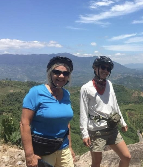 Two people wearing helmets and sunglasses in a mountainous landscape.
