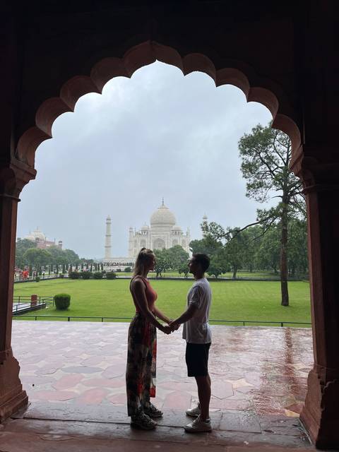 Couple holding hands under an archway with the Taj Mahal visible.