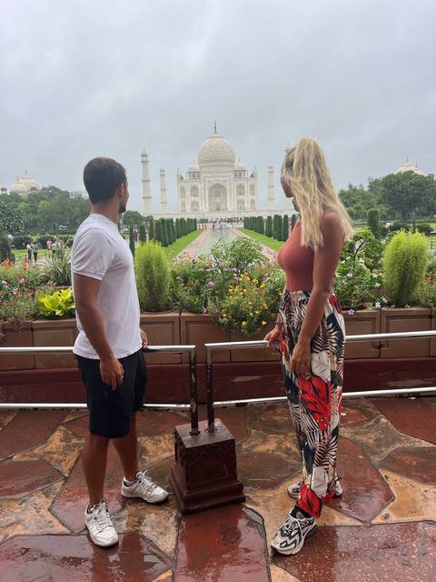 Couple standing on a terrace with the Taj Mahal visible.