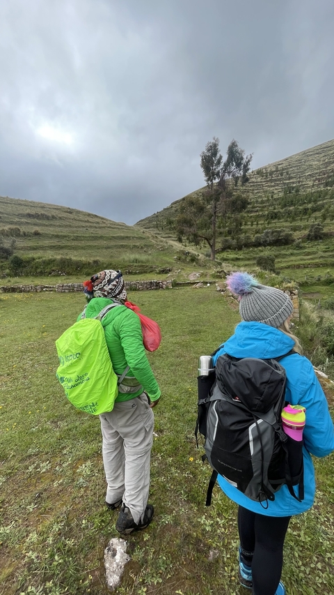 Two hikers walking through a grassy area with hills.