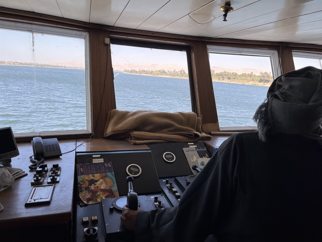 Person navigating a boat with a river and shore in view.