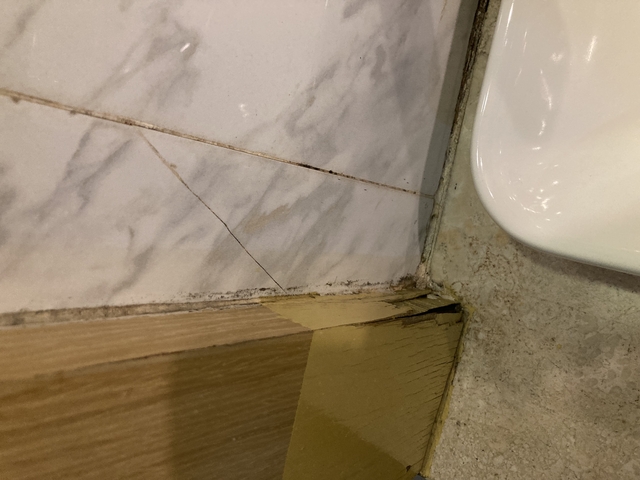       Close-up of a bathroom corner with tiles and wooden panels.
  