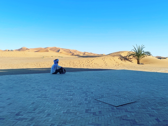 Person sitting and gazing at sand dunes in the desert.