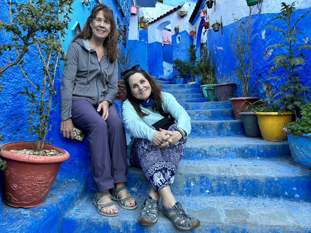 Two people sitting on blue-painted stairs in a decorated street.
