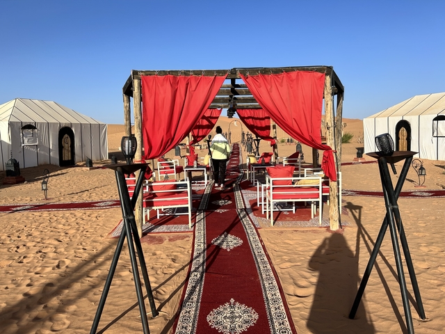       Red carpeted and tented setup in a desert camp.
  
