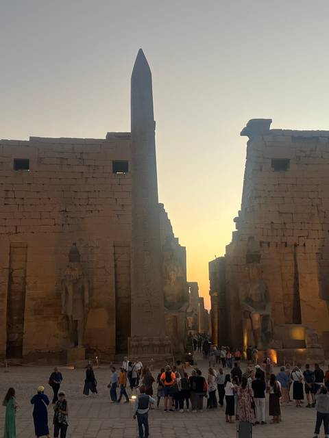Silhouette of ancient Egyptian temple at sunset with visitors.