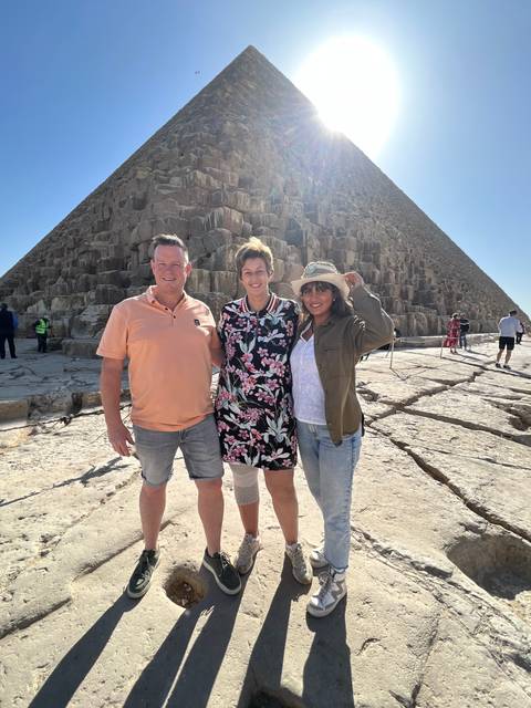 Three people standing in front of a pyramid under the sun.
