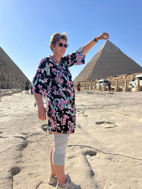       Person posing with a hand lifted, pyramid background.
  