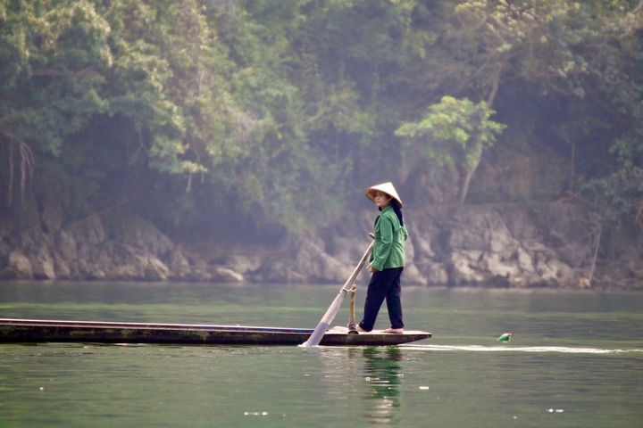       Person in traditional hat on a boat in a misty lake.
  