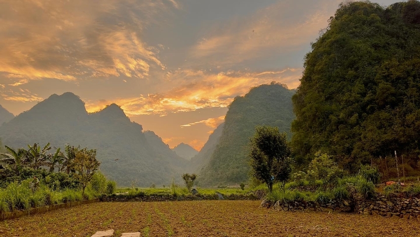       Sunset over mountains with vibrant sky and fields.
  