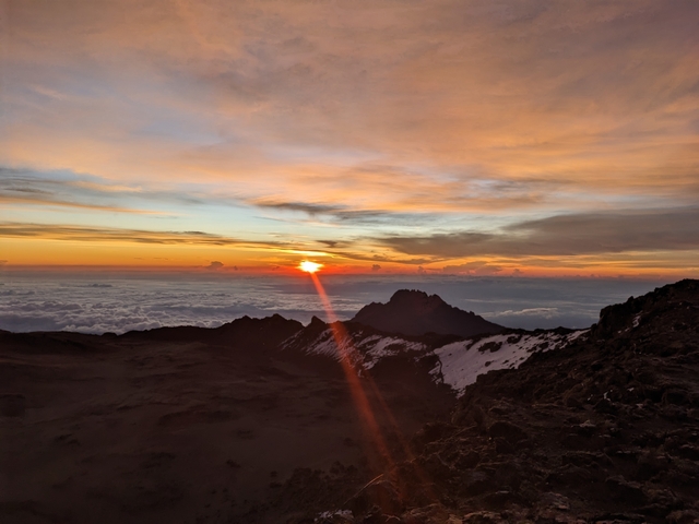 Sunrise over a mountain range with clouds below.