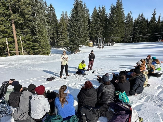 Group sitting in the snow as a person gives a talk.