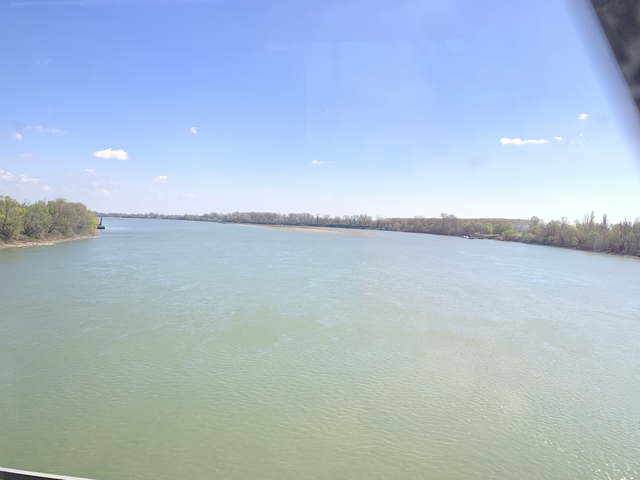 Wide river with trees on either side under a blue sky.