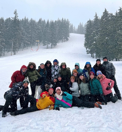 Large group of people posing on a snowy slope with trees in the background.