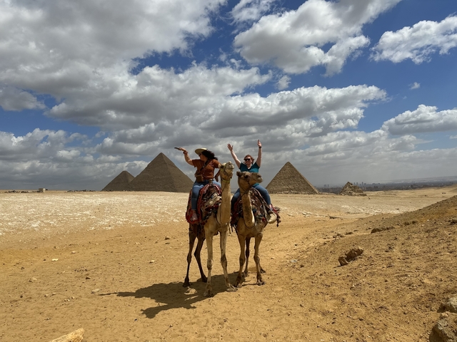 Two people on camels in front of pyramids in Giza.