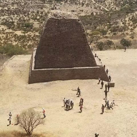       Stone pyramid with people walking around.
  