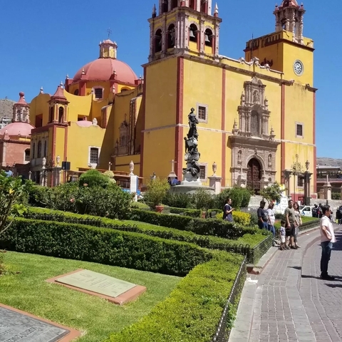       Colorful church with garden and statue.
  