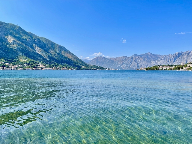       Serene view of water and mountains under clear blue sky.
  