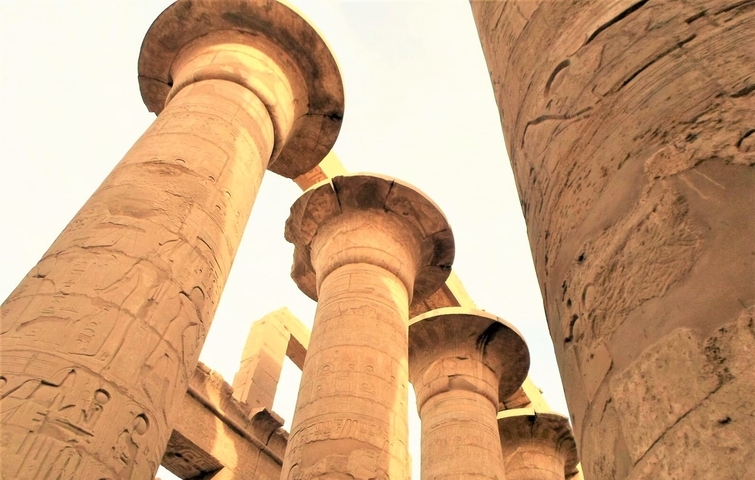       Ancient Egyptian temple columns with hieroglyphs under a bright sky.
  